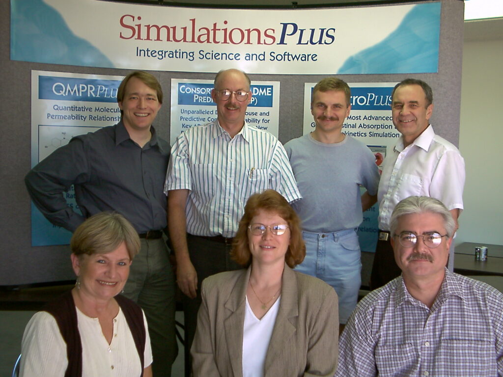 Seven colleagues pose by the "Simulations Plus: Science and Software Integration" banner in CA.